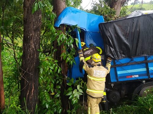 Caminhão sai da pista, bate em árvores e motorista fica preso em ferragens